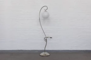 1930s Streamline Modernism floor lamp made of chrome-plated brass with a spherical opal glass shade, photographed in profile against a soft grey setting.