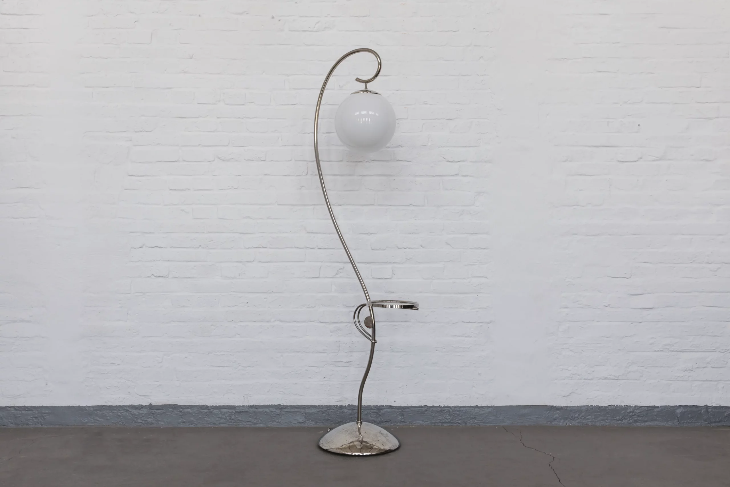1930s Streamline Modernism floor lamp made of chrome-plated brass with a spherical opal glass shade, photographed in profile against a soft grey setting.