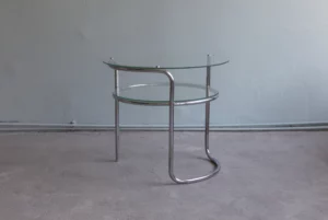 1930s tubular steel side table by Mücke-Melder with asymmetrical chromed frame and two glass tiers, photographed in a minimalist interior.