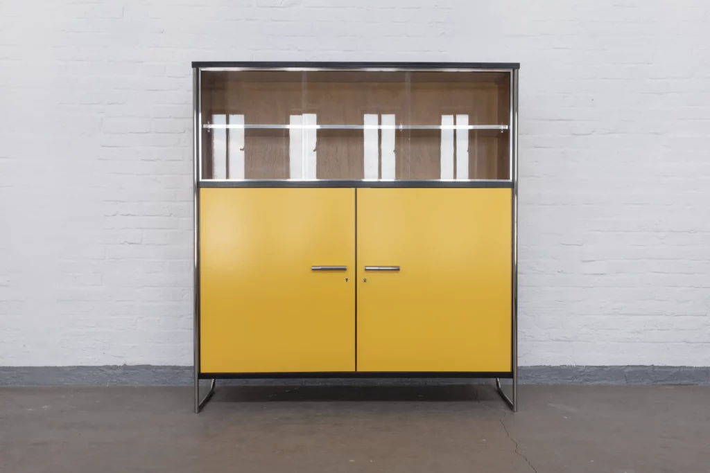 Display cabinet in the style of Bauhaus Modernism with polished tubular steel frame, sliding glass doors, yellow veneered wood panels and chrome-plated details.